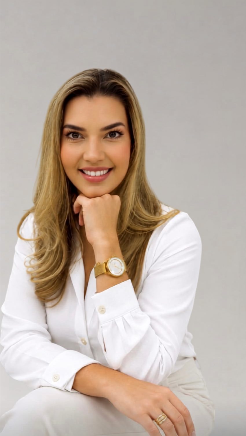 Dra. Karen Heiden sorrindo, de camisa branca, com a mão apoiada no queixo